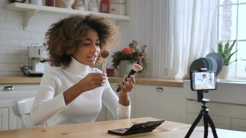 Una bloguera con pelo rizado graba un vídeo que muestra pinceles de maquillaje