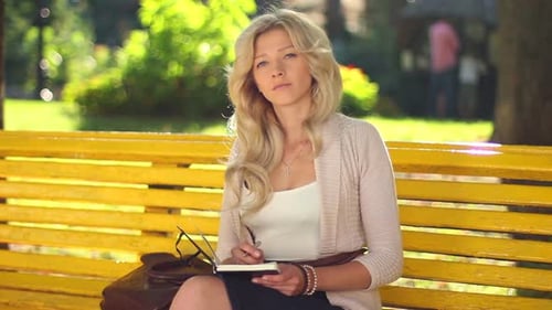 Mujer joven sentada en el banco pensando escribir notas sonriente parque