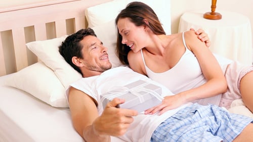Woman Gives Gift to Man in Bed