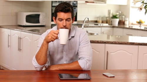 Man Using Tablet in Kitchen Drinking Coffee