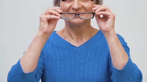 Smiling Senior Woman Puts on Eyeglasses