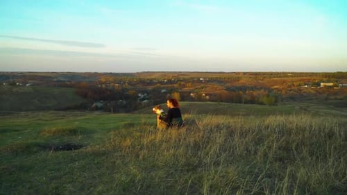 Owner and pet American Staffordshire terrier sitting on green hill at sunset