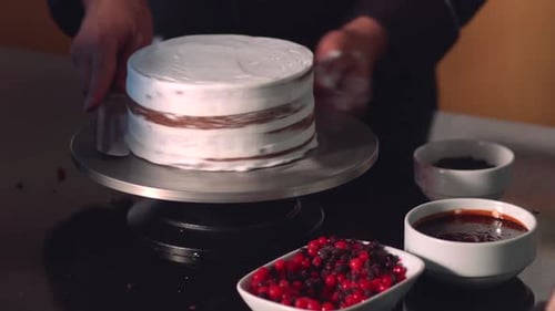 Baker Frosts Cake with White Icing and Berries