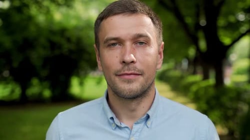 Portrait of a Young Brunette Man in a Blue Shirt in a Park