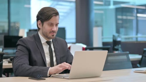 Businessman Celebrating Success While Using Laptop in Office