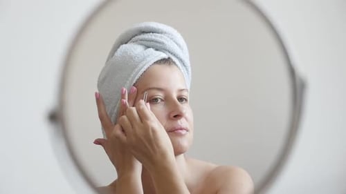 Woman Tweezing Eyebrows in Bathroom Mirror
