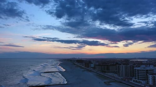 A drone shot over a quiet beach during sunset. The camera dolly out and boom down over the shore whi