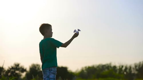 Young Boy Launches Paper Airplane in Field