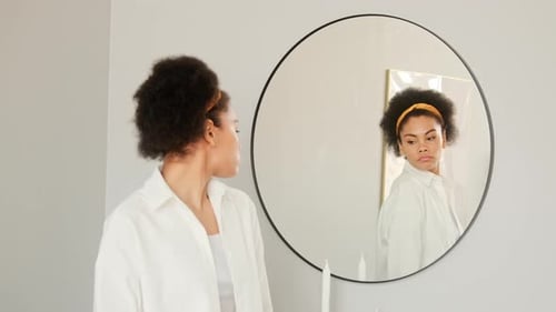 Woman Puts on Shirt in Front of Mirror