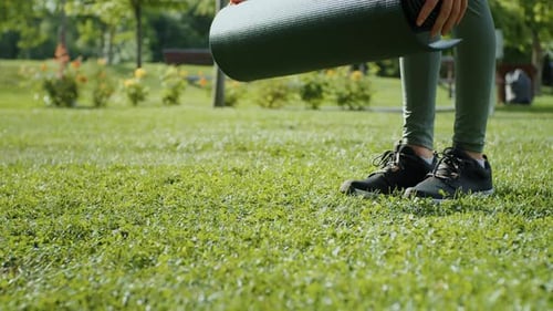 Closeup woman hands rolling up yoga mat on the grass in park.