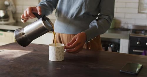 Woman Pours Coffee into Mug in Kitchen