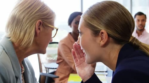 Two businesswomen whispering