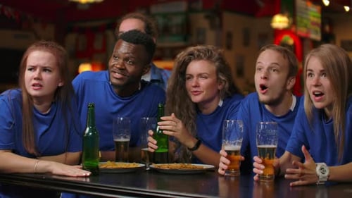 A Group of Fans of Men and Women in Blue Tshirts Rejoice Shouting and Drinking Beer at the Bar