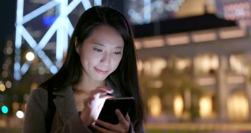 Businesswoman use of mobile phone in city in the evening