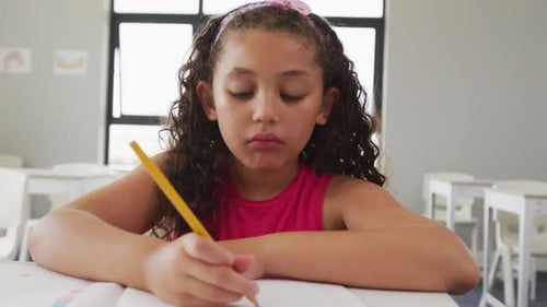 Video of happy biracial girl sitting at school desk and learning