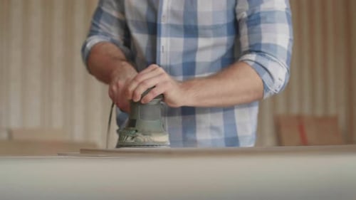Man Smoothing Wood with Power Sander in Workshop
