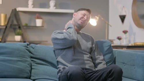 Man Massaging Sore Neck While Sitting on Couch