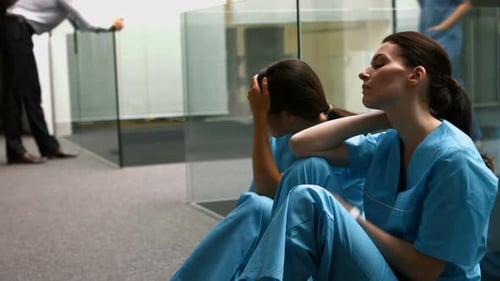 Sad nurses sitting on corridor