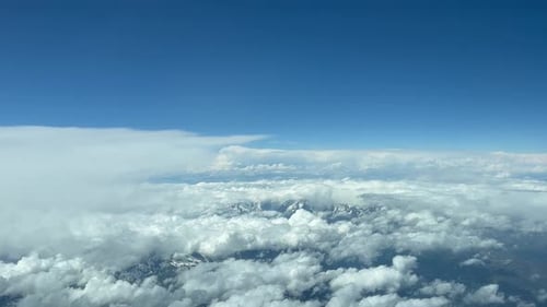 Cumulus clouds against blue sky over mountain range. Up above cloud pov airplane view