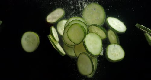 Des tranches de concombre frais tombent dans l'eau avec des bulles d'air.