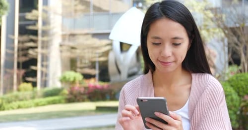 Woman Using Smartphone in Sunny Urban Park