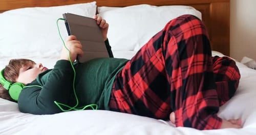 Child Lying on Bed Watching Tablet