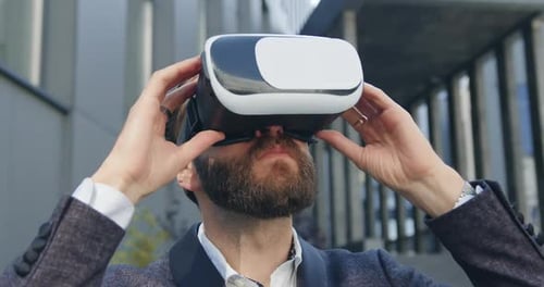 Man Putting on Virtual Reality Headset and Starting to Work Near Urban Modern building