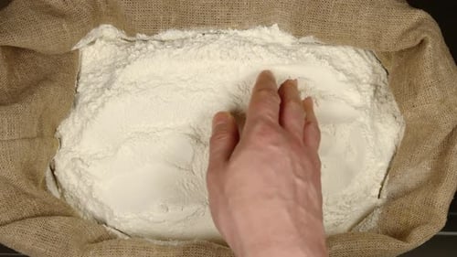 Hand Touching Flour Inside of Burlap Sack