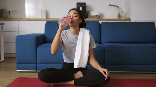 Woman drinks water and wipes face after workout