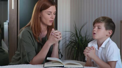 Woman and Boy Praying Together Indoors with Book