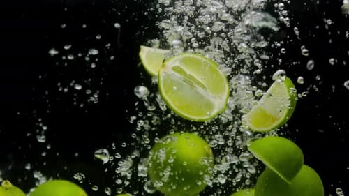 Closeup of Falling Ripe Limes Into the Sparkling Water on Black Background Making a Cocktail of
