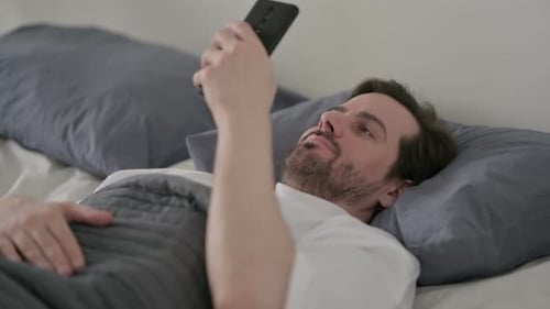 Man Lying in Bed Looking at Smartphone
