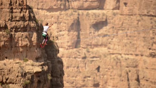 Aerial view of a woman balancing while tightrope walking and slacklining across a canyon