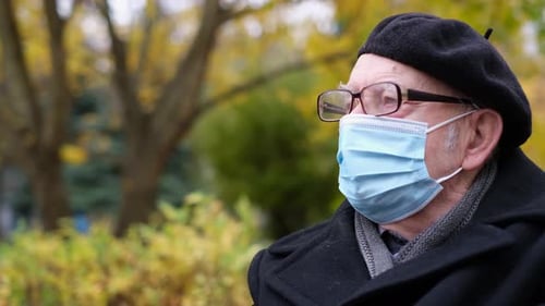 A Senior Man in a Medical Protective Mask and Goggles is Resting in the Park