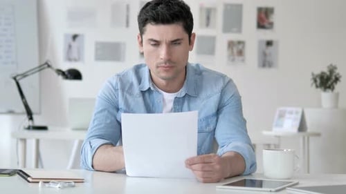 Casual Young Man Reading Documents in Office
