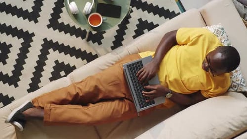 Man Typing on Laptop While Lying on Couch