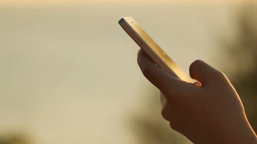 Hand Holding Phone at Sunrise or Sunset