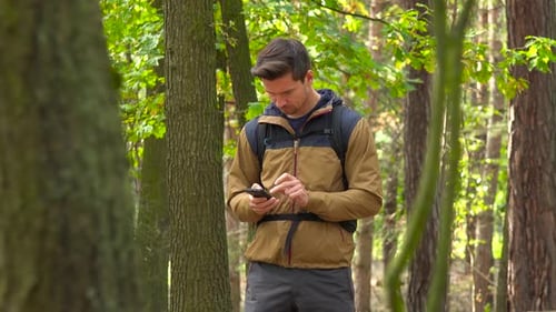 A Backpacker Works on a Smartphone in a Forest, Then Walks Off