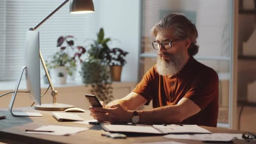 Mid-Aged Businessman Using Smartphone and Computer in Office
