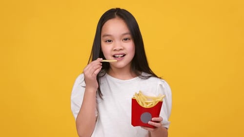 Delighted Child Eating French Fries on Yellow Background