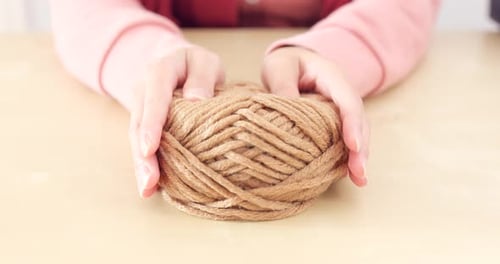 Hands Squeezing Brown Yarn Ball on Table