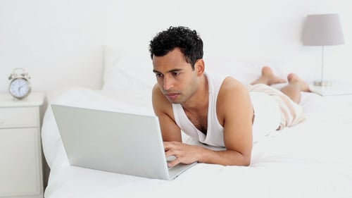 Man Lies on Bed Working on Laptop