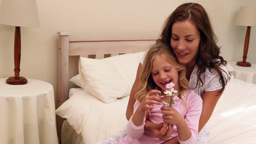 Smiling Girl with Flowers Hugs Mother in Bed