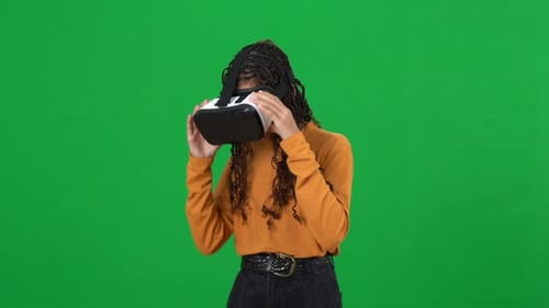 Absorbed African American Teenage Girl in VR Headset Pointing Around Turning on Green Screen