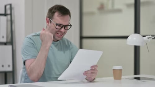 Man Cheers Reading Documents at Desk in Office
