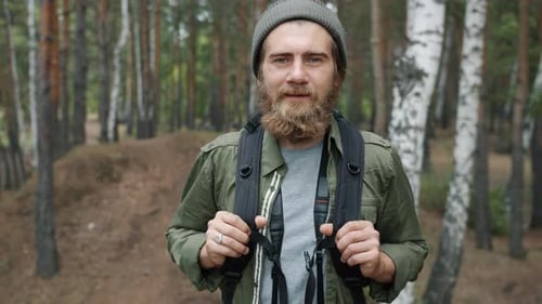 Portrait of Handsome Man Hiker Standing in Forest with Backpack and Looking at Camera