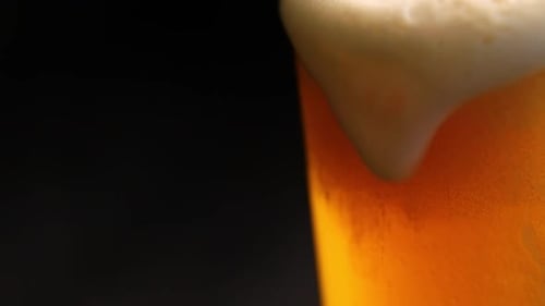 Nahaufnahme beim Biereinschenken mit Blasen und Schaum im Glas auf schwarzem Hintergrund