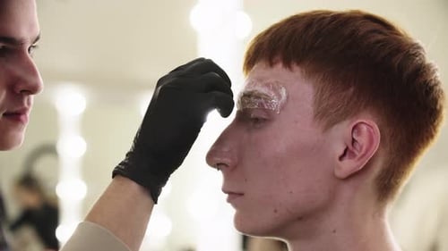 A Man Eyebrow Master Removes the Wrapping From the Eyebrow of His Male Client