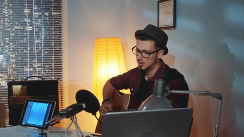 Bearded Young Man in Hat Emotionally Singing Into Microphone and Playing Guitar in Home Studio