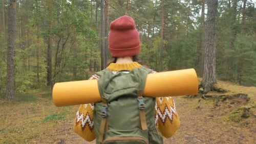 Woman with Mat in Backpack Walks Along Evergreen Forest